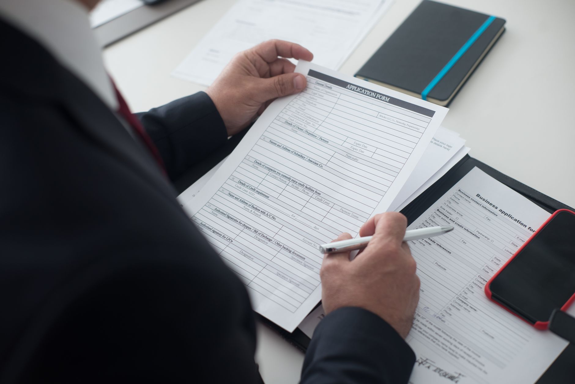 A businessman in a black suit reviews a printed application form with a pen on his desk. — CAO College Applications - Top 10