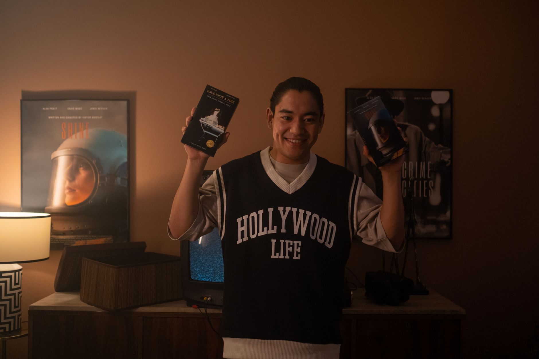 Smiling man holding vintage VHS tapes, standing in a warmly lit room with classic movie posters. — Curated Movie Posters for