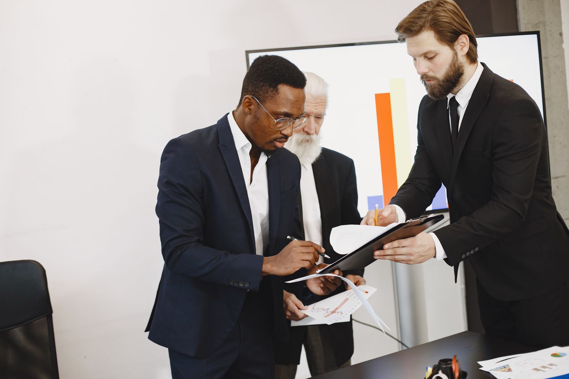 Three businessmen engaged in document signing in a modern office setting. — Why You Should Buy weed online