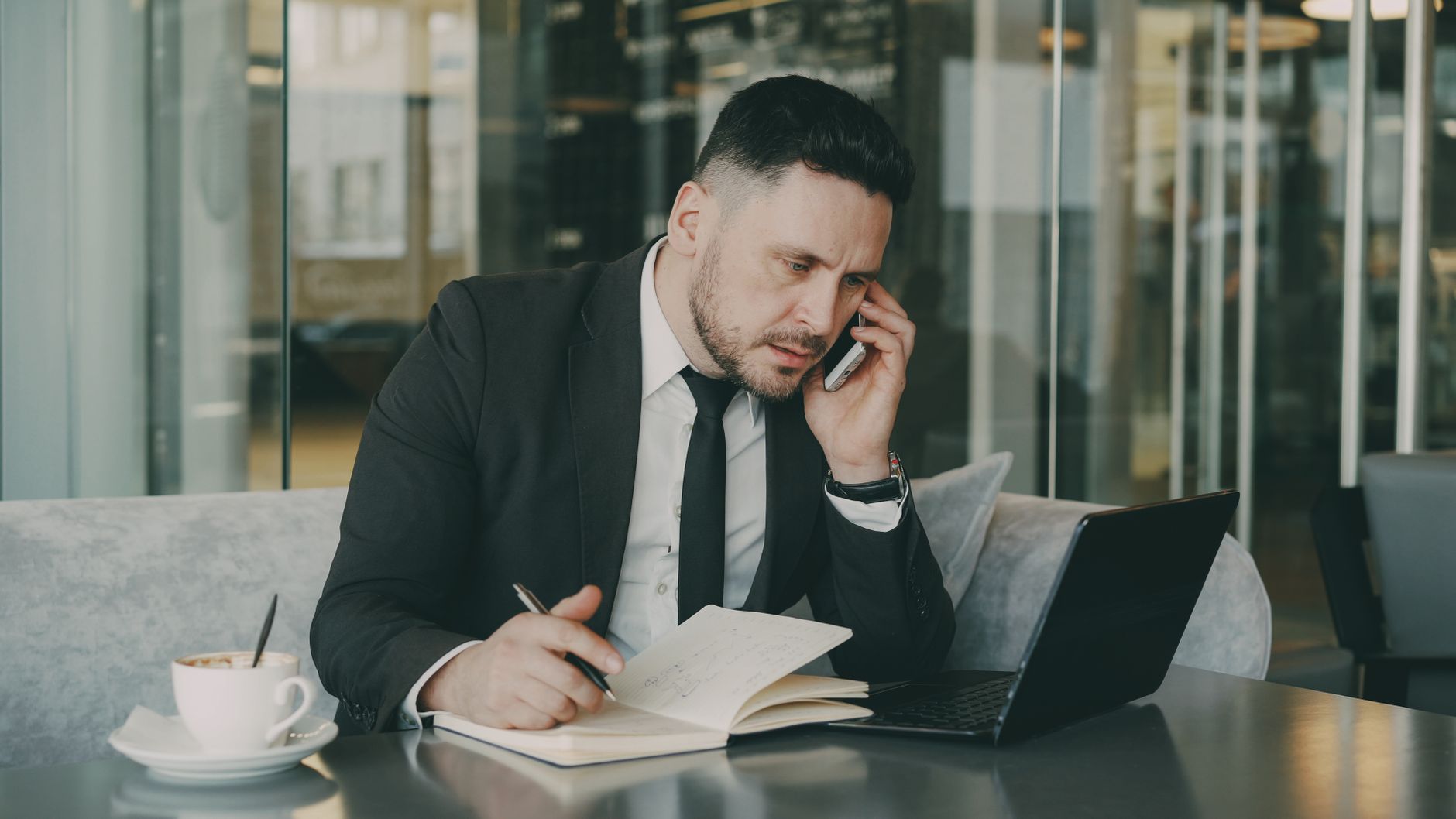 Businessman talks on phone while writing notes in a modern cafe. — The Benefits Of Working With A Financial Advisor By Vincen