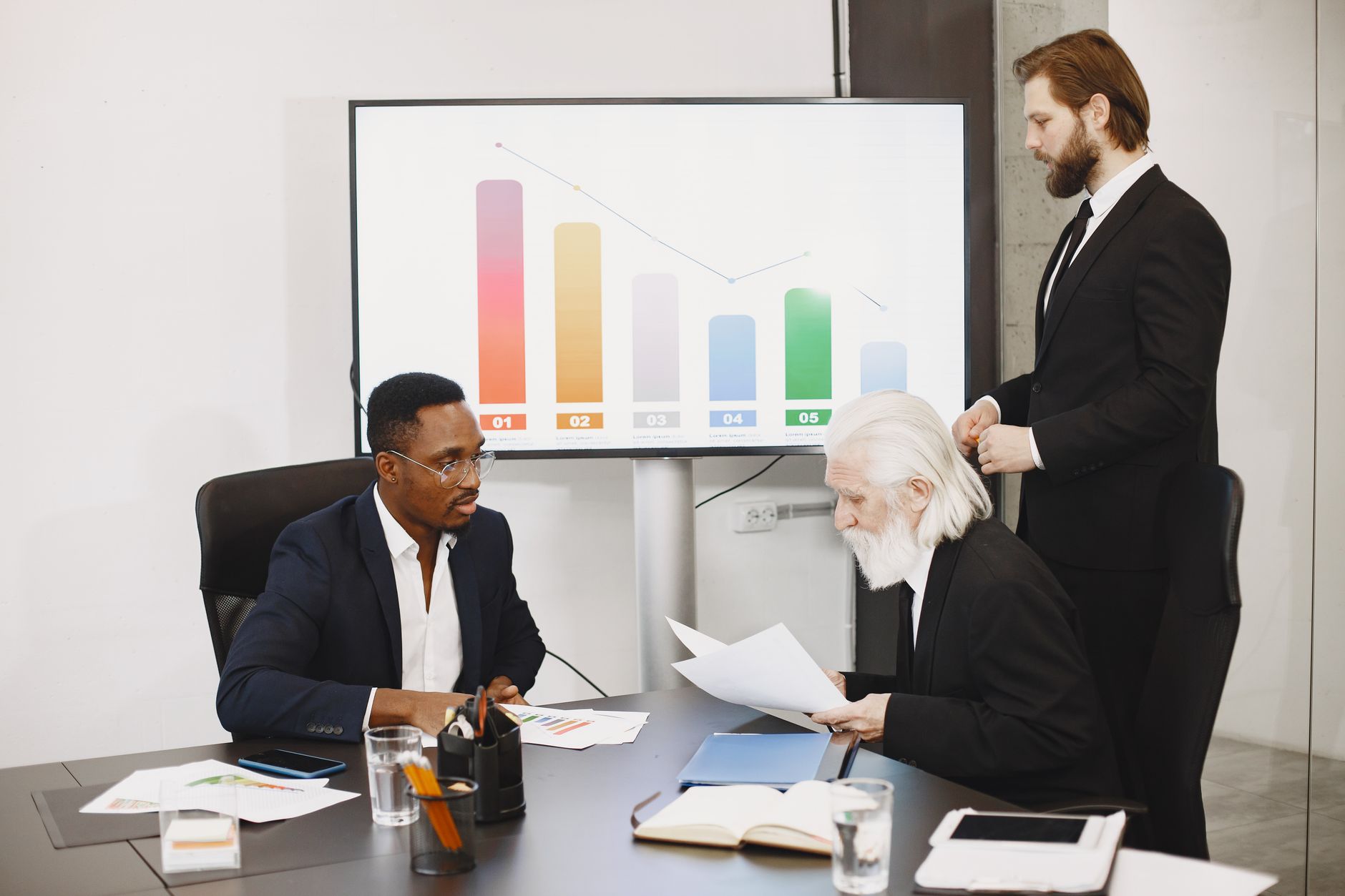 Three businessmen discussing financial data in a modern office setting with charts. — What are the Biggest SEO Trends in 2020