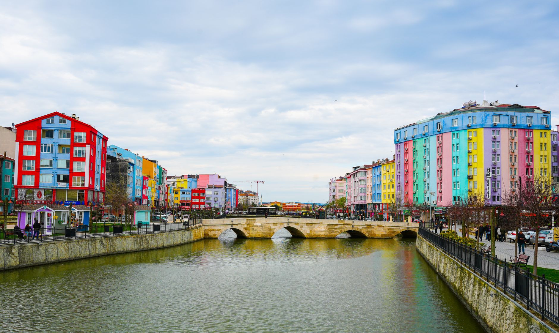 Vibrant cityscape with colorful buildings along a river and stone bridge under a cloudy sky. — Why gamble on football online?